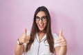 Young brunette woman wearing glasses standing over pink background approving doing positive gesture with hand, thumbs up smiling Royalty Free Stock Photo