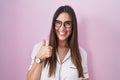 Young brunette woman wearing glasses standing over pink background doing happy thumbs up gesture with hand Royalty Free Stock Photo