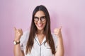 Young brunette woman wearing glasses standing over pink background success sign doing positive gesture with hand, thumbs up Royalty Free Stock Photo