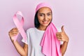 Young brunette woman wearing head scarf and holding pink cancer ribbon smiling happy and positive, thumb up doing excellent and Royalty Free Stock Photo