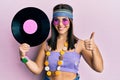 Young brunette woman wearing hippie style holding vinyl disc smiling happy and positive, thumb up doing excellent and approval Royalty Free Stock Photo