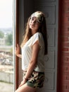 Young brunette woman, wearing jersey pajamas, standing neat big window in dark room in the morning. Hen party celebration. Fashion