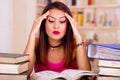 Young brunette woman wearing pink top sitting by desk with stack of books placed on it, holding hands onto head, tired Royalty Free Stock Photo