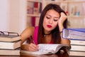 Young brunette woman wearing pink top sitting by desk with stack of books placed on it, resting head onto hand, tired Royalty Free Stock Photo
