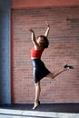 Young brunette woman, wearing red top and black leather skirt, dancing posing in spacious studio loft room with huge window. Royalty Free Stock Photo