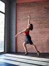 Young brunette woman, wearing red top and black leather skirt, dancing posing in spacious studio loft room with huge window. Royalty Free Stock Photo