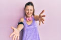 Young brunette woman wearing sportswear and headphones looking at the camera smiling with open arms for hug Royalty Free Stock Photo