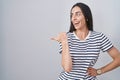 Young brunette woman wearing striped t shirt smiling with happy face looking and pointing to the side with thumb up Royalty Free Stock Photo