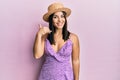 Young brunette woman wearing summer dress and hat smiling doing phone gesture with hand and fingers like talking on the telephone Royalty Free Stock Photo