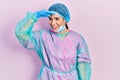 Young brunette woman wearing surgeon uniform and medical mask very happy and smiling looking far away with hand over head