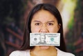 Young brunette woman wearing white sweater covering mouth with twenty dollar bill, facing camera, hostage concept