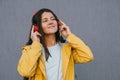 Young brunette woman wearing yellow raincoat and using red headphones listening music during walking outdoor against gray Royalty Free Stock Photo