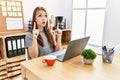 Young brunette woman working at the office with laptop amazed and surprised looking up and pointing with fingers and raised arms Royalty Free Stock Photo