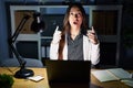 Young brunette woman working at the office at night with laptop amazed and surprised looking up and pointing with fingers and Royalty Free Stock Photo