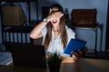 Young brunette woman working at the office at night smiling and laughing with hand on face covering eyes for surprise Royalty Free Stock Photo