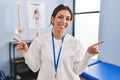 Young brunette woman working at pain recovery clinic smiling confident pointing with fingers to different directions