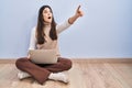 Young brunette woman working using computer laptop sitting on the floor pointing with finger surprised ahead, open mouth amazed Royalty Free Stock Photo
