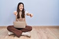 Young brunette woman working using computer laptop sitting on the floor pointing to you and the camera with fingers, smiling Royalty Free Stock Photo