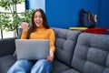 Young brunette woman working using computer laptop sitting on the sofa pointing thumb up to the side smiling happy with open mouth Royalty Free Stock Photo