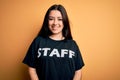Young brunette worker woman wearing staff t-shirt as uniform over yellow isolated background with a happy face standing and Royalty Free Stock Photo