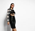 Young brutal brunette woman in checkered jacket, black leather skirt, cross-belt and narrow sunglasses is sexy posing