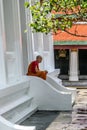 Young Buddhist monk resting on the stairs of Grand Palace temple. Ancient architecture of Asia. Sights of Bangkok.