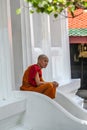 Young Buddhist monk resting on the stairs of Grand Palace temple. Ancient architecture of Asia. Sights of Bangkok.