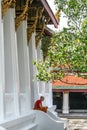 Young Buddhist monk resting on the stairs of Grand Palace temple. Ancient architecture of Asia. Sights of Bangkok.