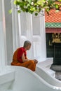 Young Buddhist monk resting on the stairs of Grand Palace temple. Ancient architecture of Asia. Sights of Bangkok.