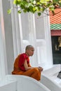 Young Buddhist monk resting on the stairs of Grand Palace temple. Ancient architecture of Asia. Sights of Bangkok.