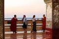 Young buddhist monks dressed in traditional red clothes talking with female tourists at sunset time. All barefoot. Su Taung Pyae