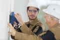 Young builder apprentice in hardhat sanding wall indoors