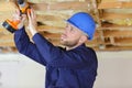 Young builder drilling wooden ceiling joist