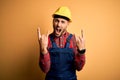 Young builder man wearing construction uniform and safety helmet over yellow isolated background shouting with crazy expression
