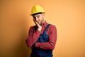 Young builder man wearing construction uniform and safety helmet over yellow isolated background thinking looking tired and bored