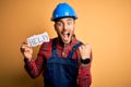 Young builder man wearing safety helmet offering help and support over yellow background screaming proud and celebrating victory Royalty Free Stock Photo