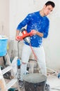 young builder mixing plaster in bucket using electric mixer