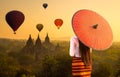 A young Burmese woman is walking with a red umbrella. Young girl and Sunrise many hot air balloon with stupas in Bagan, Myanmar. Royalty Free Stock Photo