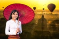 A young Burmese woman is walking with a red umbrella. Young girl and Sunrise many hot air balloon with stupas in Bagan, Myanmar. Royalty Free Stock Photo