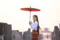 A young Burmese woman is walking with a red umbrella on the longest teak bridge in Asia.U-bein bridge, Mandalay, Myanmar