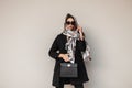 Young business fashion woman in stylish sunglasses in a black coat with a fashionable leather handbag in glamour scarf posing near Royalty Free Stock Photo
