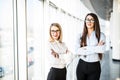 Young business ladies in office hall over panoramic windows. Royalty Free Stock Photo