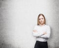 Young business lady with crossed hands. Concrete wall.