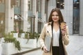 Young business lady holding laptop under arm walking down the street near office center with cup of coffee looking busy, eating on Royalty Free Stock Photo