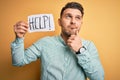 Young business man with blue eyes asking for help holding paper note over yellow background serious face thinking about question, Royalty Free Stock Photo