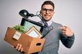 Young business man with blue eyes holding box from the office beeing fired from job with surprise face pointing finger to himself Royalty Free Stock Photo