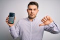 Young business man with blue eyes holding dataphone payment terminal over isolated background with angry face, negative sign Royalty Free Stock Photo