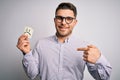 Young business man with blue eyes holding paper note with sad face as unhappy message with surprise face pointing finger to Royalty Free Stock Photo