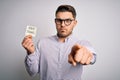 Young business man with blue eyes holding pay taxes word on paper note pointing with finger to the camera and to you, hand sign, Royalty Free Stock Photo