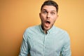 Young business man with blue eyes wearing elegant green shirt over yellow background afraid and shocked with surprise expression, Royalty Free Stock Photo